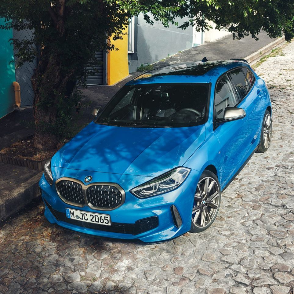 Nuova BMW Serie 1 a bordo strada. Nuova BMW Serie 1 in Misano Blue metallizzato, vista anteriore a tre quarti parcheggiata a bordo strada con prospettiva a volo di uccello.
