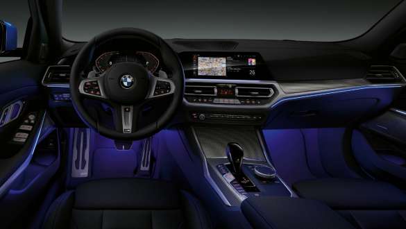BMW Serie 3 Berlina, Ambient Light Vista anteriore del cockpit lato guida della BMW Serie 3 Berlina con vano piedi illuminato in blu dall’Ambient Light.
