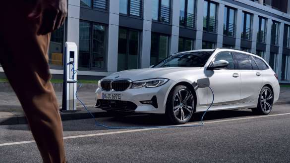 BMW Serie 3 Touring ibrida Plug-in 2021 G21 Vista anteriore a tre quarti in ricarica BMW Serie 3 Touring ibrida Plug-in 2021 G21 Vista anteriore a tre quarti in ricarica davanti ad un edificio