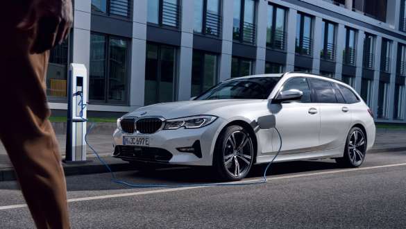 BMW Serie 3 Touring ibrida Plug-in 2021 G21 Vista anteriore a tre quarti in ricarica BMW Serie 3 Touring ibrida Plug-in 2021 G21 Vista anteriore a tre quarti in ricarica davanti a un edificio