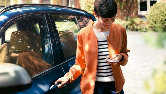BMW TeleServices BMW Teleservice Donna al volante con smartphone vicino alla portiera della BMW