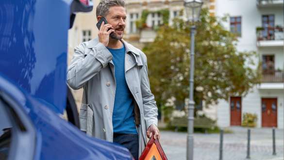 Uomo vicino al vano bagagli della BMW Serie 5 Berlina G30 Uomo con Smartphone e triangolo di sosta vicino al vano bagagli della BMW Serie 5 Berlina G30