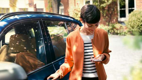 Donna con smartphone e BMW Serie 5 Berlina G30 Donna scende dalla BMW Serie 5 Berlina G30 guardando lo smartphone