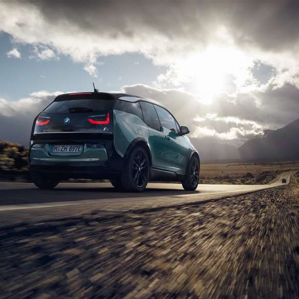 BMW i3 2018 vista posteriore a tre quarti in viaggio su una strada provinciale I01 BMW i3 I01 2018 Jucaro Beige con profilo in Frozen Grey metallizzato vista posteriore a tre quarti in viaggio su una strada provinciale