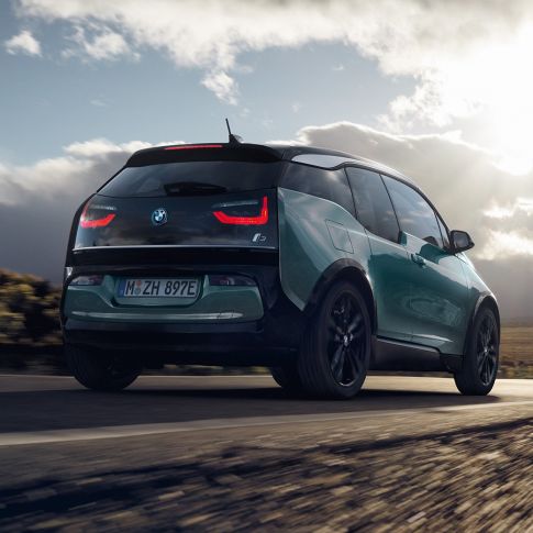 BMW i3 2018 Jucaro Beige vista posteriore a tre quarti in viaggio su una strada provinciale I01 BMW i3 I01 2018 Jucaro Beige con profilo in Frozen Grey metallizzato vista posteriore a tre quarti in viaggio su una strada provinciale