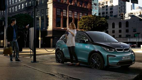 BMW i3 2018 presso una stazione di ricarica pubblica in Jucaro Beige con profilo in Frozen Grey metallizzato I01 Una coppia ricarica la propria BMW i3 presso una stazione di ricarica pubblica I01 2018 in Jucaro Beige con profilo in Frozen Grey metallizzato