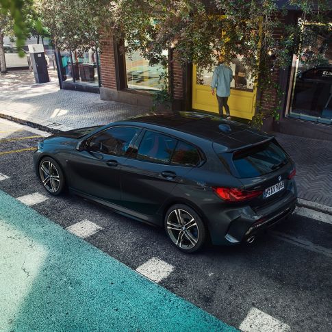 BMW M135i xDrive, mentre sta parcheggiando F40. BMW M135i xDrive in Sapphire Black metallizzato, vista laterale con prospettiva a volo di uccello, mentre sta parcheggiando F40.