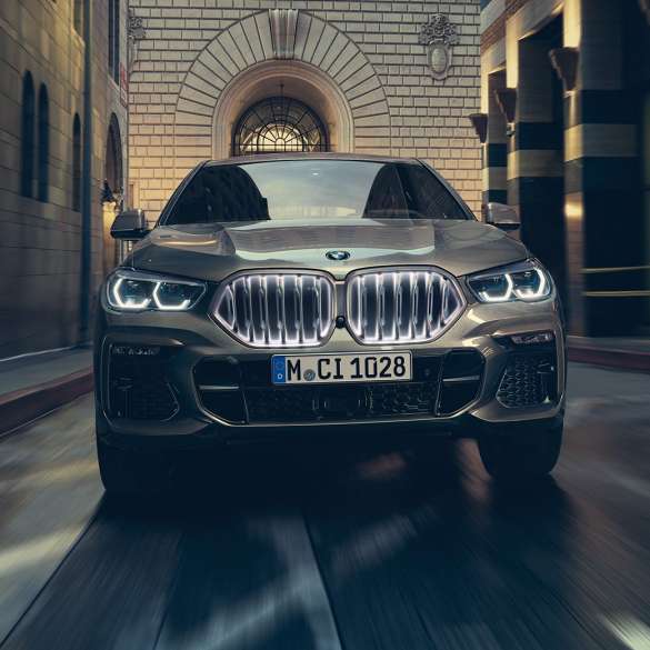 BMW X6 M50i con doppio rene BMW “Iconic Glow”. Vista anteriore della BMW X6 M50i in ambiente urbano.