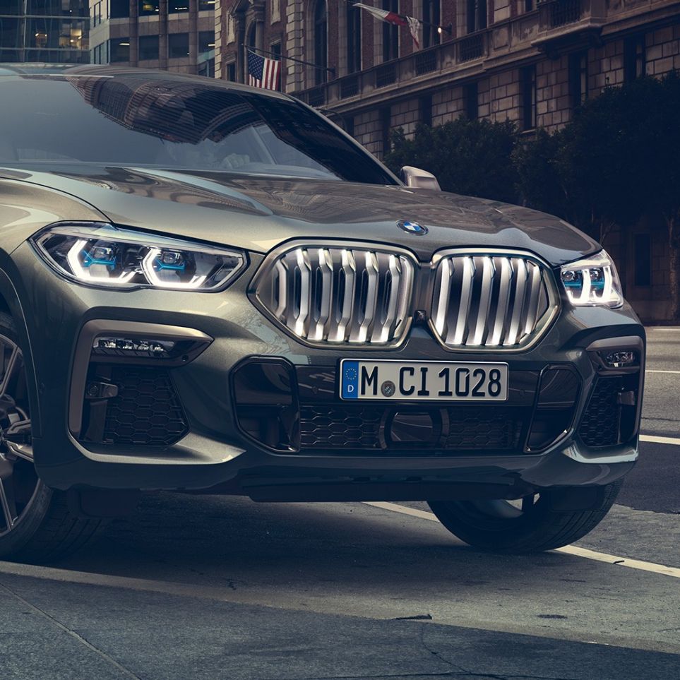 BMW X6 M50i ferma. Vista anteriore a tre quarti ferma della BMW X6 M50i in ambiente urbano.