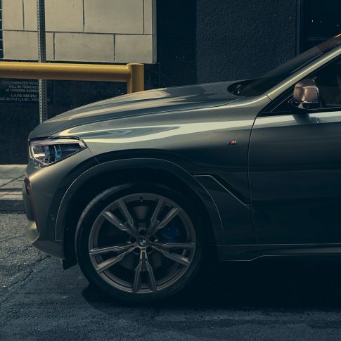 BMW X6 M50i in vista laterale. Vista laterale di un uomo appoggiato alla BMW X6 M50i in ambiente urbano.