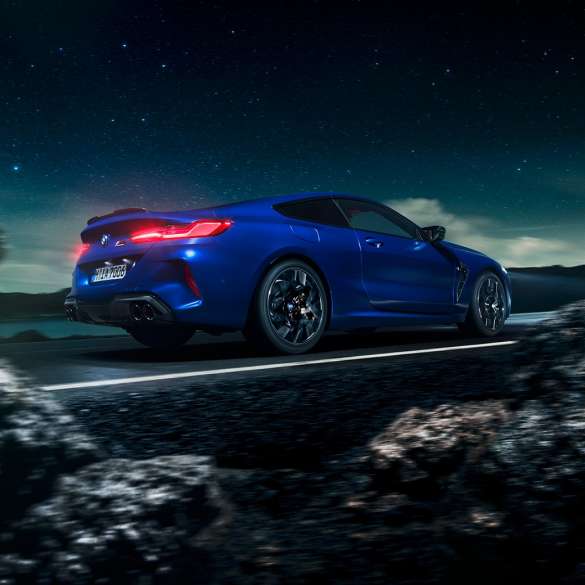 BMW M8 M Coupé, vista laterale di tre quarti. BMW M8 Competition Coupé in Marina Bay Blue metallizzato, vista laterale di tre quarti con auto in marcia davanti al cielo stellato.