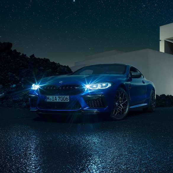 BMW M8 M Competition Coupé, vista frontale di tre quarti F92. BMW M8 Competition Coupé in Marina Bay Blue metallizzato con fari a LED accesi, vista frontale di tre quarti in sosta davanti a una villa di notte F92.
