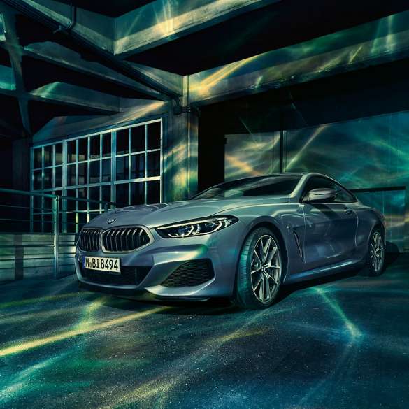 BMW M850i xDrive Coupé, vista frontale di tre quarti G15. BMW M850i xDrive Coupé in Barcelona Blue metallizzato, vista frontale di tre quarti in sosta davanti a un edificio G15.