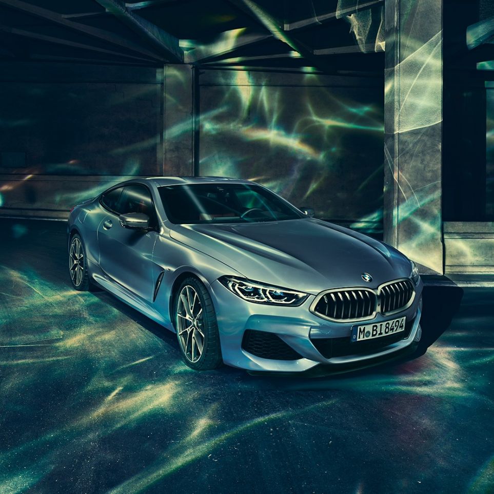 BMW M850i xDrive Coupé, vista frontale di tre quarti da sinistra G15. BMW M850i xDrive Coupé in Barcelona Blue metallizzato, vista frontale di tre quarti da sinistra, in sosta davanti a un edificio G15.