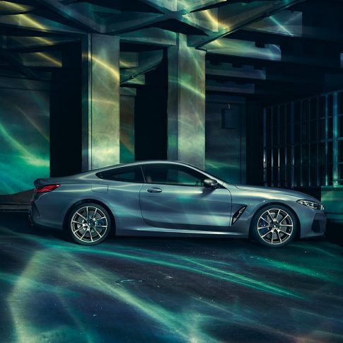 BMW M850i xDrive Coupé, vista laterale G15. BMW M850i xDrive Coupé in Barcelona Blue metallizzato, vista laterale, in sosta davanti a un edificio G15.