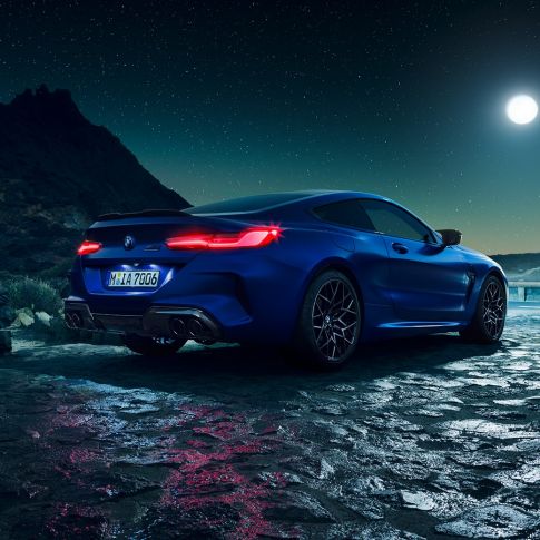 BMW M8 M Coupé, vista posteriore di tre quarti F92. BMW M8 Competition Coupé in Marina Bay Blue metallizzato con gruppi ottici posteriori a LED accesi, vista posteriore di tre quarti in sosta con la luna piena F92.