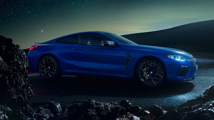 BMW M8 M Coupé, vista laterale di tre quarti F92. BMW M8 Competition Coupé in Marina Bay Blue metallizzato, vista laterale di tre quarti con auto in sosta di notte F92.