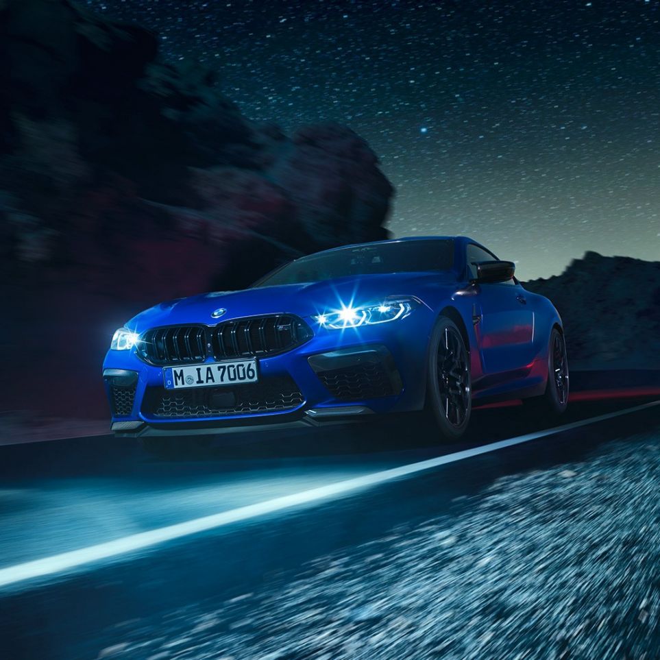 BMW M8 M Coupé in marcia, vista frontale di tre quarti F92. BMW M8 Competition Coupé in Marina Bay Blue metallizzato con fari a LED accesi, vista frontale di tre quarti, in marcia di notte F92.