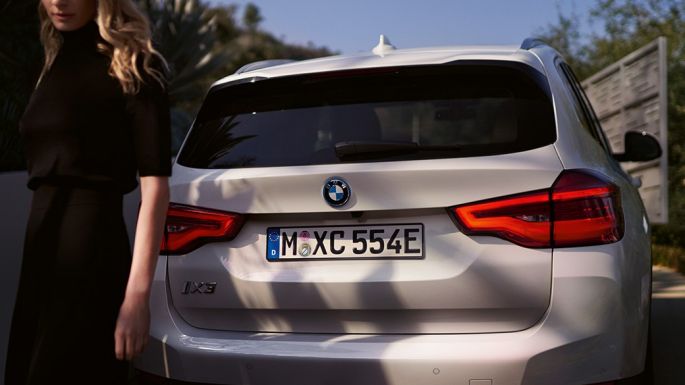 Posteriore con diffusore specifico delle virione BMW i della BMW iX3 G08 2020 vista posteriore con donna Posteriore con diffusore specifico delle veroni BMW i della BMW iX3 G08 2020 Mineral White metallizzato vista posteriore con donna