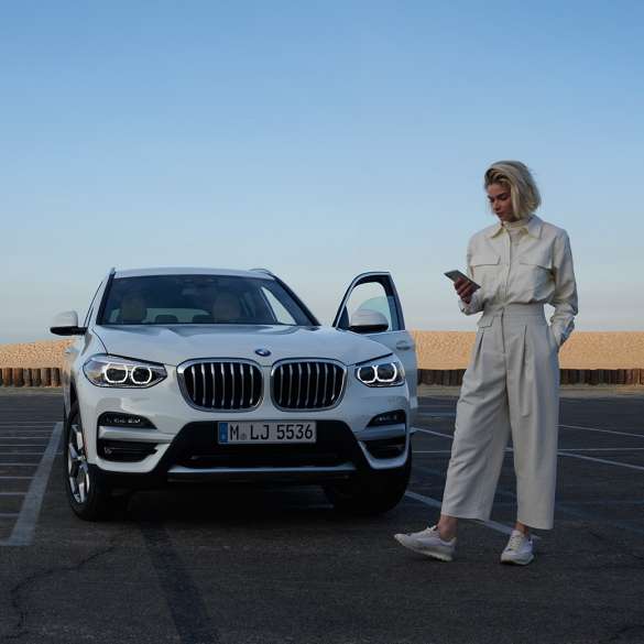 Una donna utilizza l’app My BMW sul proprio smartphone Una donna utilizza l’app My BMW di BMW ConnectedDrive sul proprio smartphone davanti alla BMW X5