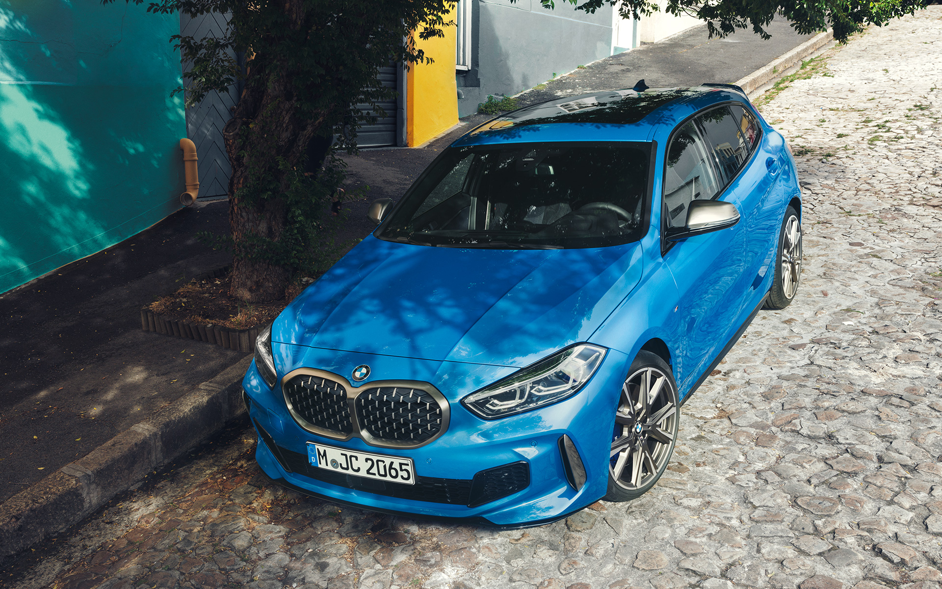 BMW Serie 1 M135i F40 a bordo strada BMW Serie 1 M135i F40 in Misano Blue metallizzato, vista anteriore a tre quarti parcheggiata a bordo strada con prospettiva a volo di uccello