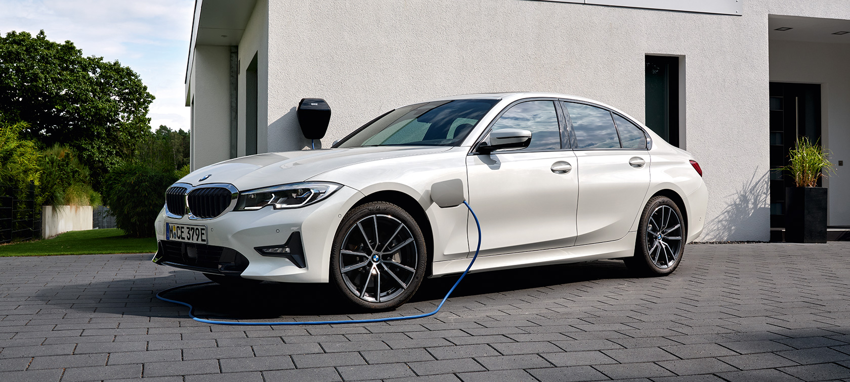BMW Serie 3 Berlina ibrida Plug-in 2021 G20 G20 Vista laterale a tre quarti in ricarica BMW Serie 3 Berlina ibrida Plug-in 2021 G20 Vista laterale a tre quarti in ricarica davanti al garage