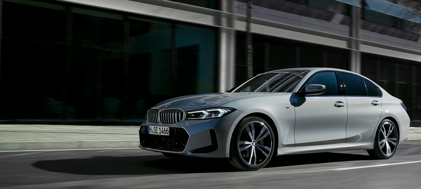 Vista laterale da ferma della BMW Serie 3 Berlina LCI G20 Brooklyn Grey davanti a una parete