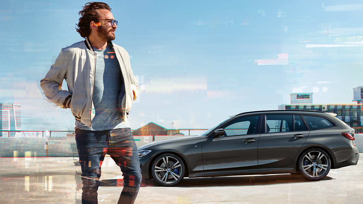 BMW Serie 3 Touring (G21), ripresa anteriore del design BMW Serie 3 Touring (G21) Dravit Grey, vista anteriore a tre quarti mentre attraversa un ponte rurale