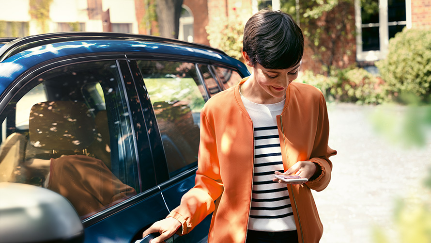 BMW Service Donna con smartphone davanti alla propria BMW BMW Service Donna con smartphone davanti alla propria BMW