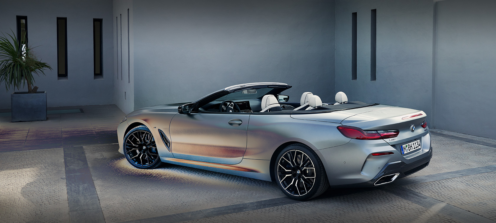 Un uomo appoggiato alla BMW Serie 8 Cabrio G14 LCI Facelift 2022 BMW Individual BMW Individual Frozen Pure Grey metallizzato Vista laterale da ferma davanti a un edificio