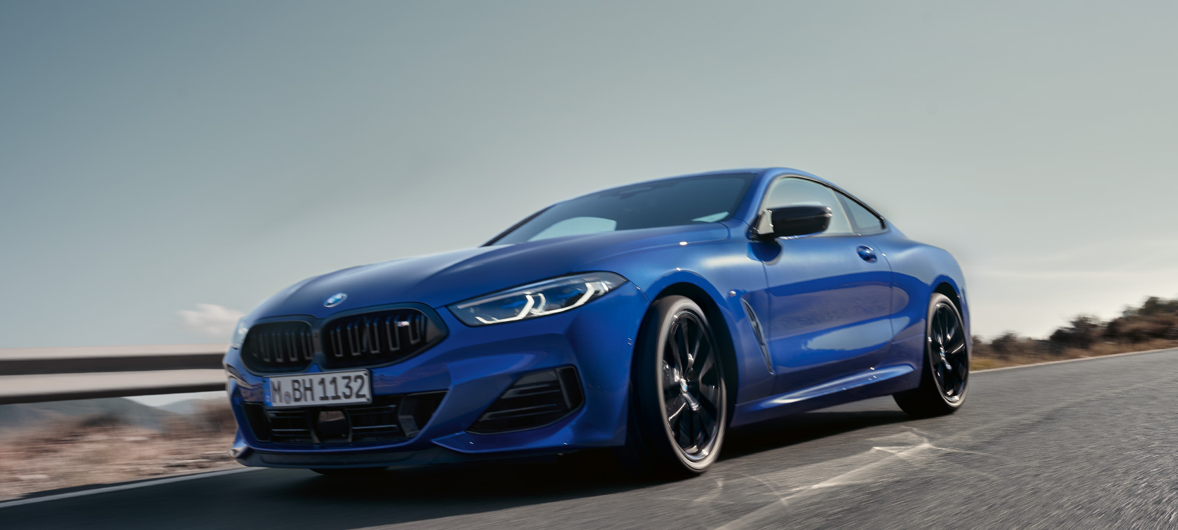 BMW Serie 8 Coupé G15 LCI Facelift 2022 BMW M850i xDrive M Portimao Blue metallizzato vista anteriore con prospettiva dal basso in movimento BMW Serie 8 Coupé G15 LCI Facelift 2022 BMW M850i xDrive M Portimao Blue metallizzato vista anteriore con prospettiva dal basso in movimento su strada provinciale con paesaggio collinare