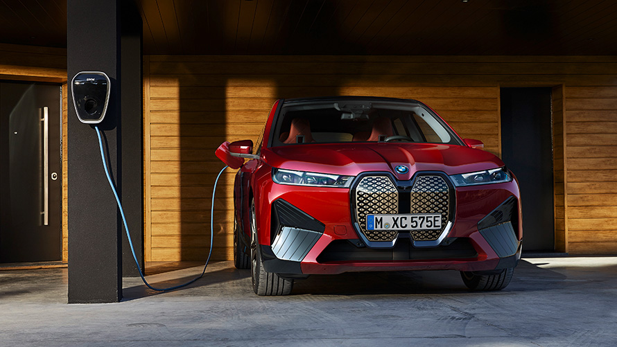 SUV elettrico BMW iX i20 SUV BMW iX xDrive50 Ricarica SUV elettrico BMW iX i20 2021 BMW iX xDrive50 Aventurine Red in ricarica vicino ad una BMW Wallbox Ricarica