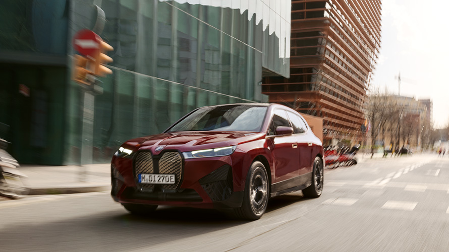 SUV elettrico BMW iX i20 BMW iX xDrive50 assistenza alla guida SUV elettrico BMW iX i20 2021 BMW iX xDrive50 Aventurine Red Vista in movimento con sfondo urbano