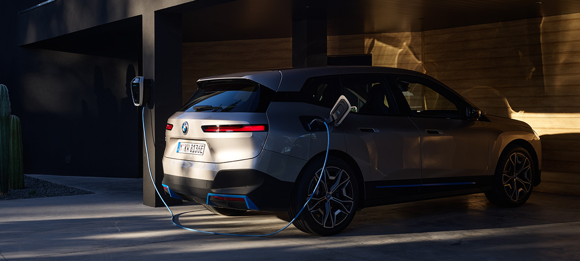 BMW iX vista posteriore tre quarti con BMW Wallbox BMW iX Cashmere Silver i20 vista posteriore tre quarti in carica con BMW Wallbox