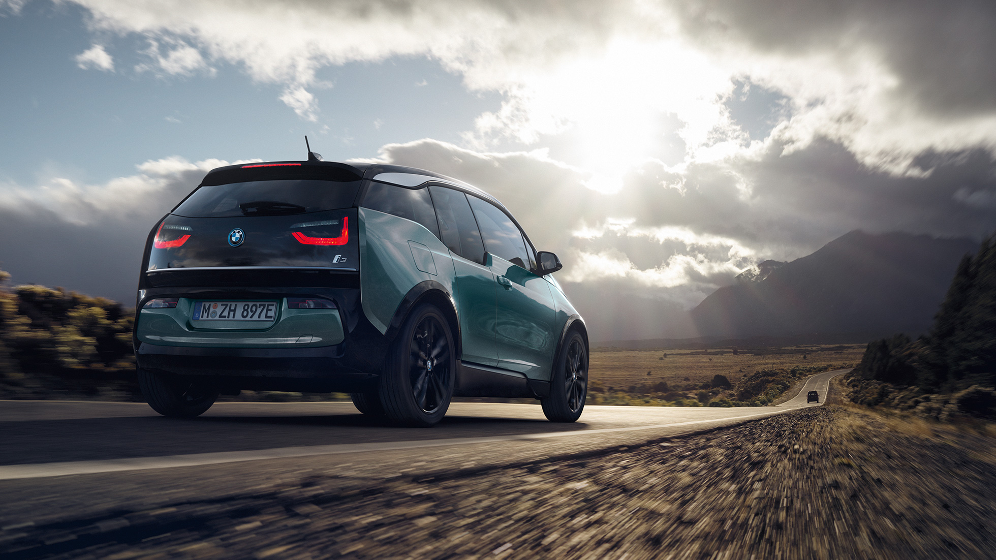 BMW i3 2018 vista posteriore a tre quarti in viaggio su una strada provinciale I01 BMW i3 I01 2018 Jucaro Beige con profilo in Frozen Grey metallizzato vista posteriore a tre quarti in viaggio su una strada provinciale