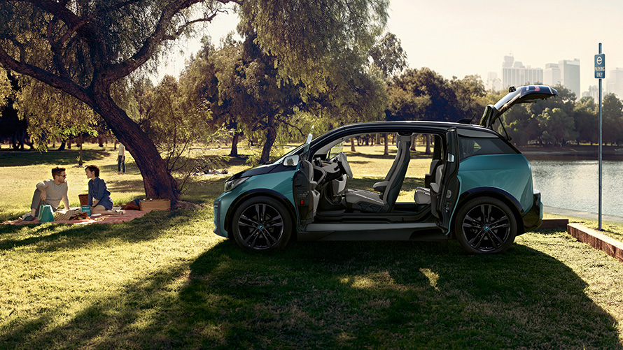 BMW i3 2018 in un parco I01 BMW i3 I01 2018 Jucaro Beige con profilo in Frozen Grey metallizzato vista laterale con porte aperte in un parco