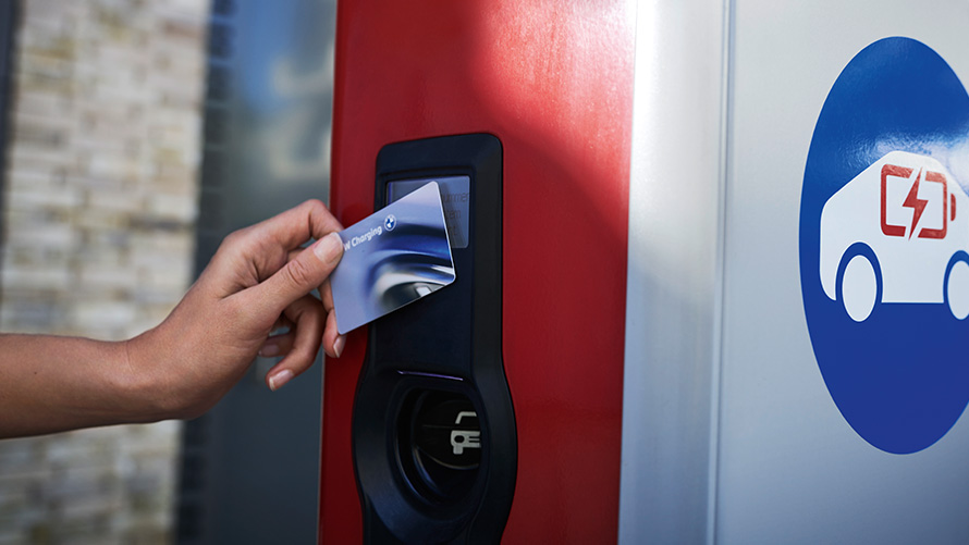 Una persona presso una colonnina di ricarica pubblica tiene in mano la BMW Charging Card Una persona presso una colonnina di ricarica pubblica tiene in mano la BMW Charging Card