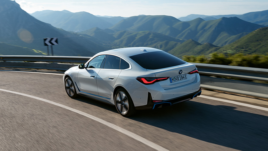 Vista posteriore a tre quarti della BMW i4 eDrive40 G26 2021 in movimento BMW i4 eDrive40 G26 2021 Mineral White Vista posteriore a tre quarti in movimento