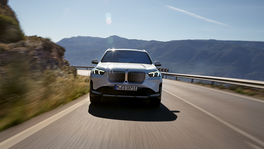 Vista anteriore in movimento della BMW iX1 U11 BEV 2022 Mineral White su strada di montagna