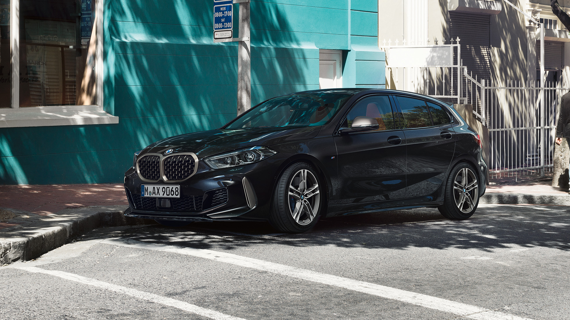BMW M135i xDrive, vista laterale a tre quarti F40. BMW M135i xDrive in Sapphire Black metallizzato, vista laterale a tre quarti, mentre sta parcheggiando F40.