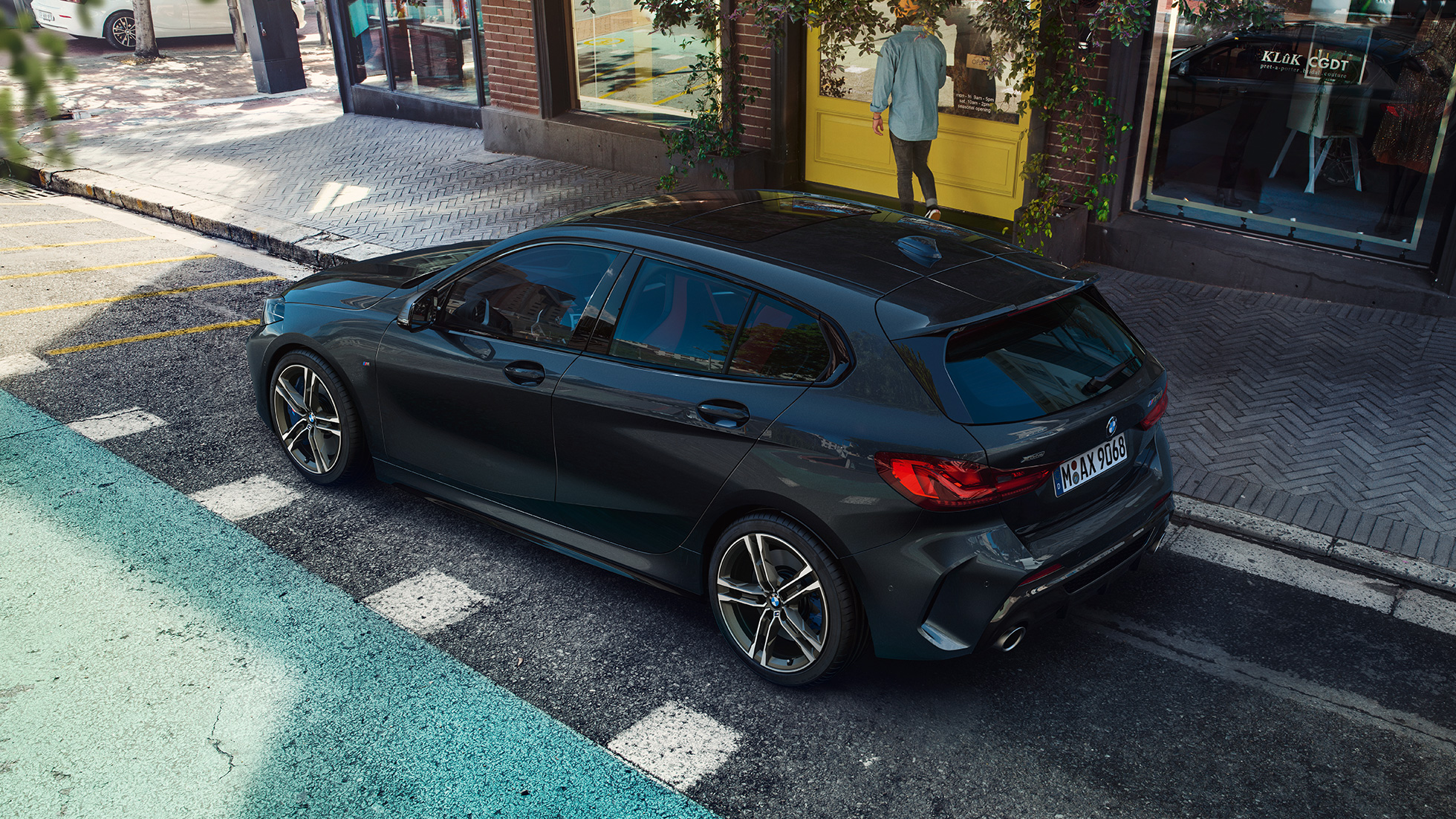 BMW M135i xDrive, mentre sta parcheggiando F40. BMW M135i xDrive in Sapphire Black metallizzato, vista laterale con prospettiva a volo di uccello, mentre sta parcheggiando F40.