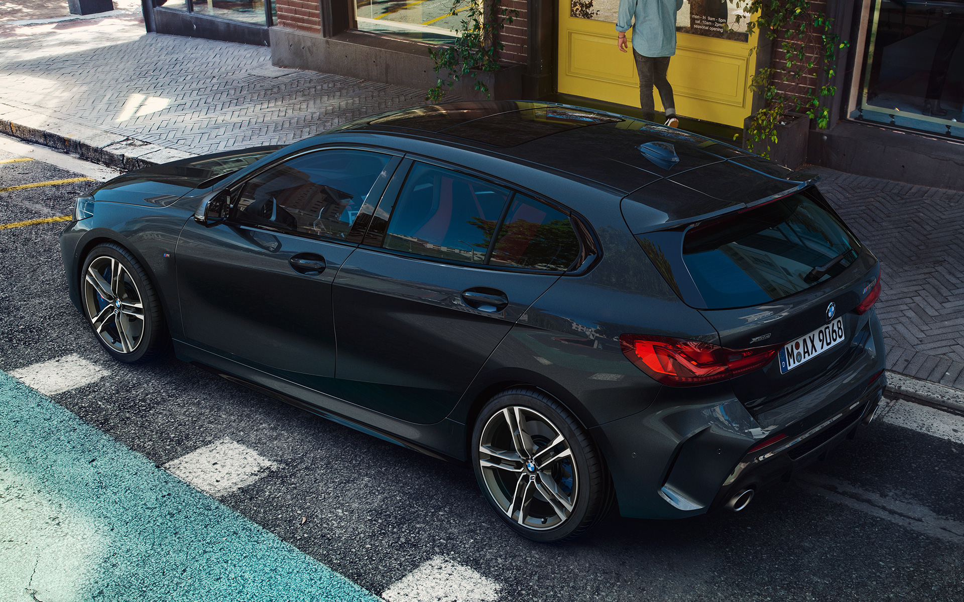 BMW M135i xDrive (F40) in Sapphire Black metallizzato parcheggiata, vista laterale con prospettiva a volo di uccello