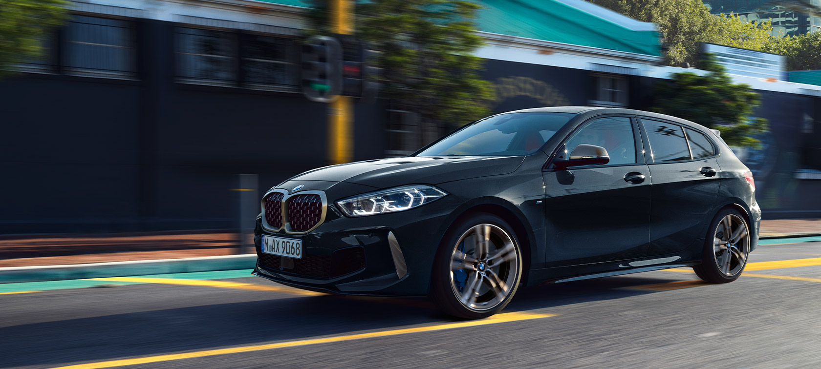 BMW Serie 1 M135i xDrive (F40) in Sapphire Black metallizzato auto in movimento con sfondo urbano