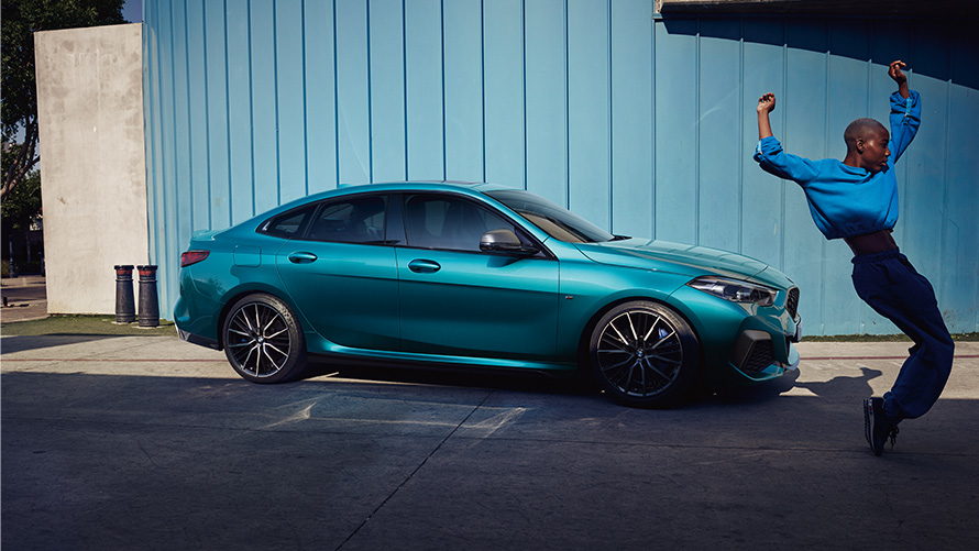 BMW M235i xDrive Gran Coupé F44 vista laterale con donna in primo piano BMW M235i xDrive Gran Coupé F44 Snapper Rocks Blue metallizzato vista laterale con donna in primo piano