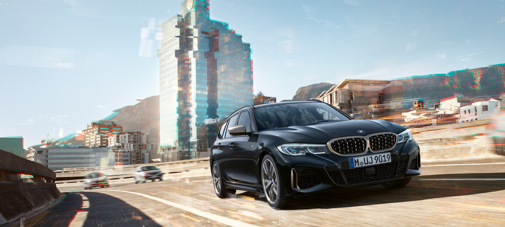 Vista anteriore a tre quarti in movimento in ambiente urbano Nuova BMW M340i xDrive Touring, vista anteriore a tre quarti in movimento in ambiente urbano
