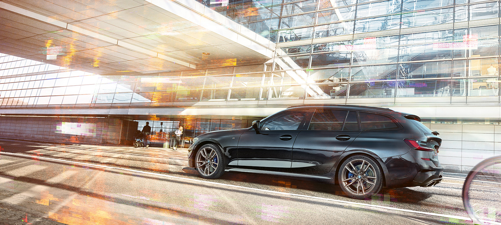 Nuova BMW M340i xDrive Touring, ripresa laterale in movimento Nuova BMW M340i xDrive Touring, ripresa laterale in movimento davanti a un edificio con facciate in vetro
