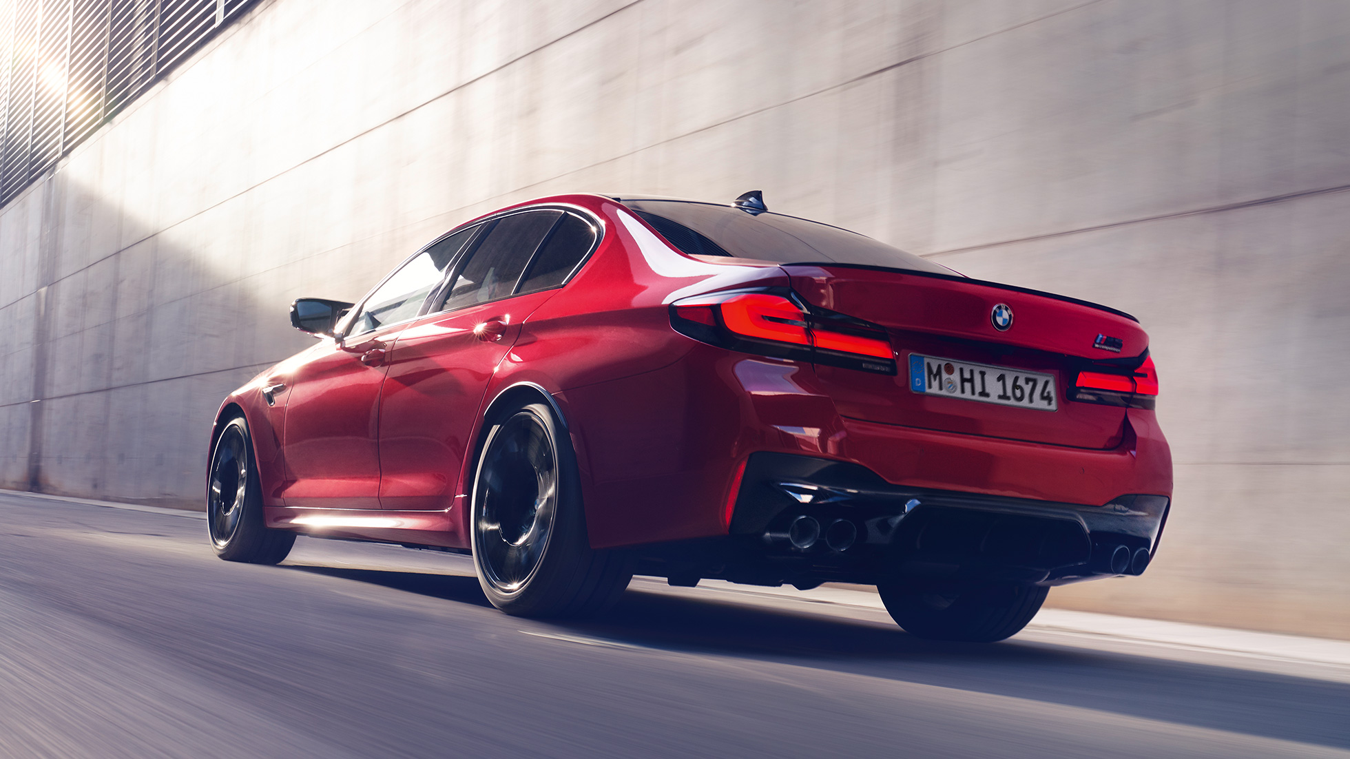 BMW M5 Competition F90 LCI Facelift 2020 vista posteriore a tre quarti BMW M5 Competition F90 LCI Facelift 2020 BMW Individual Imola Red vista posteriore a tre quarti in movimento