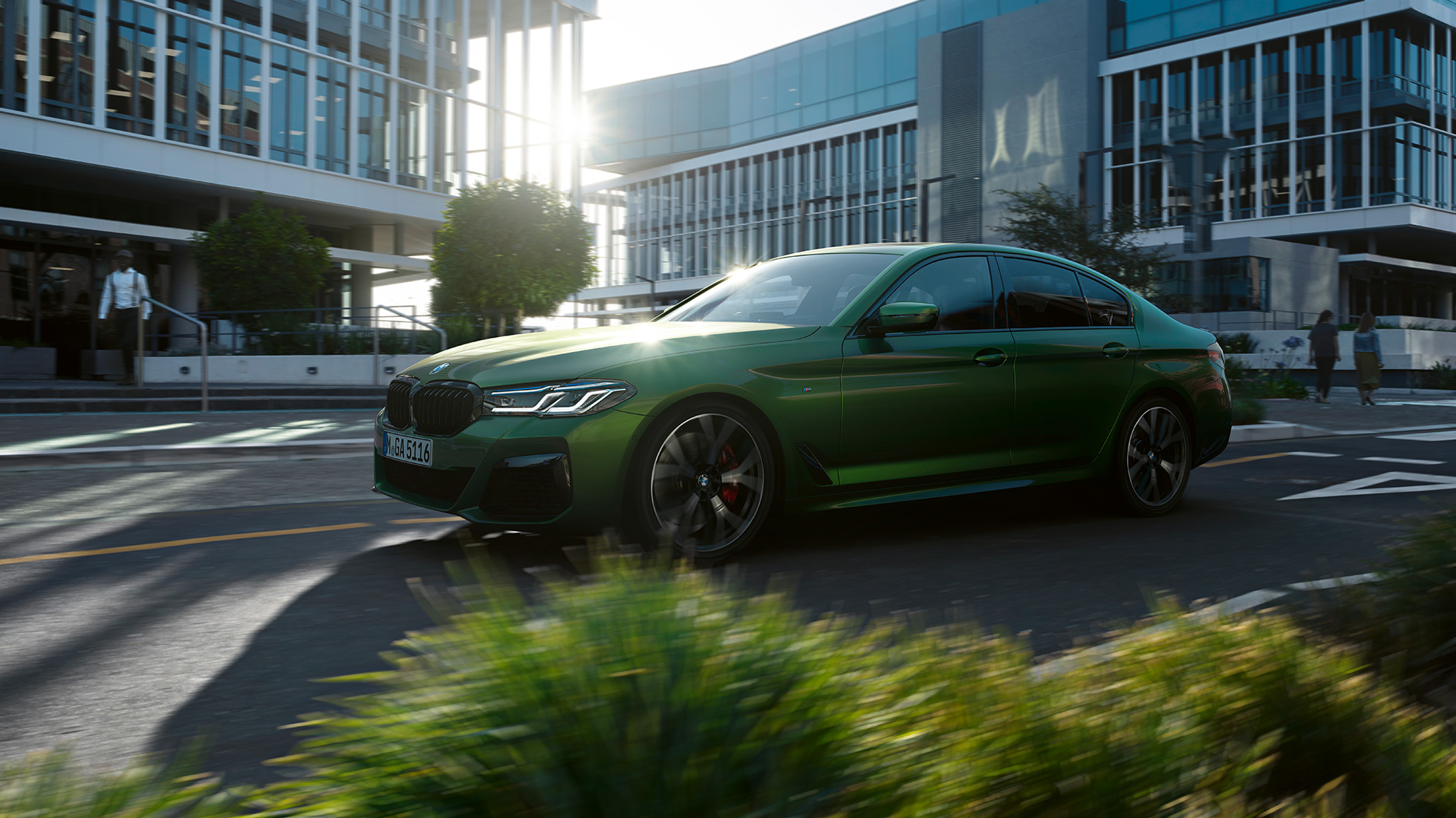BMW M550i xDrive Berlina G30 LCI Facelift 2020 vista laterale in movimento BMW M550i xDrive Berlina G30 LCI Facelift 2020 Hermes Green BMW Individual metallizzato vista laterale in movimento su strada in ambiente urbano
