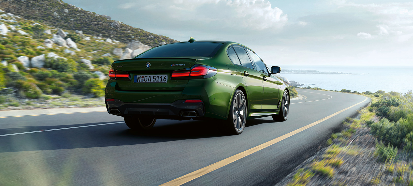 BMW M550i xDrive Berlina G30 LCI Facelift 2020 vista posteriore a tre quarti in movimento BMW M550i xDrive Berlina G30 LCI Facelift 2020 Hermes Green BMW Individual metallizzato vista posteriore a tre quarti in movimento