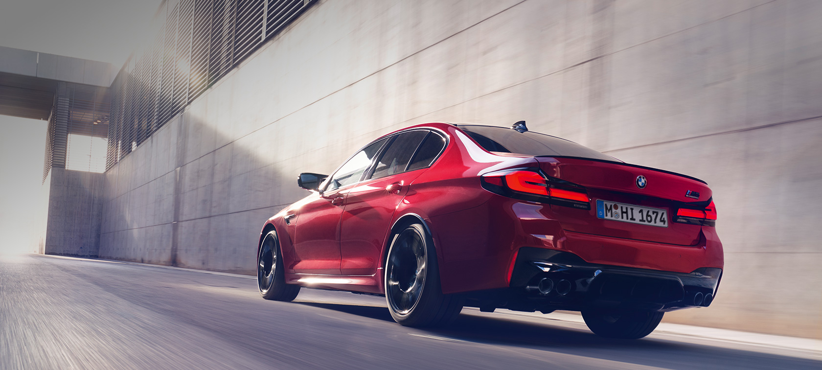 BMW M5 Competition F90 LCI Facelift 2020 vista posteriore a tre quarti in movimento BMW M5 Competition F90 LCI Facelift 2020 BMW Individual Imola Red vista posteriore a tre quarti in movimento